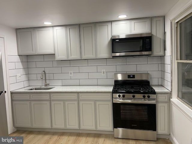 kitchen with decorative backsplash, sink, stainless steel appliances, and light hardwood / wood-style flooring