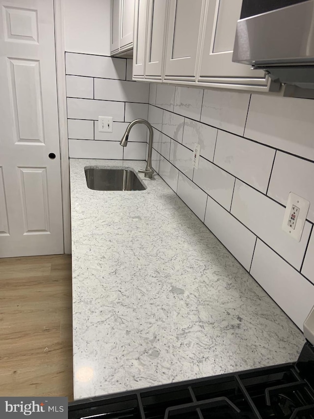 kitchen featuring light stone countertops, white cabinetry, sink, and tasteful backsplash