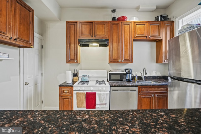 kitchen with appliances with stainless steel finishes, dark stone countertops, and sink