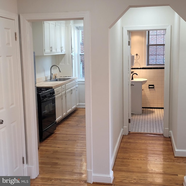 kitchen featuring white cabinets, sink, light hardwood / wood-style flooring, and black range with gas cooktop