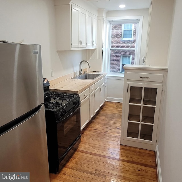 kitchen with gas stove, stainless steel fridge, white cabinetry, and sink