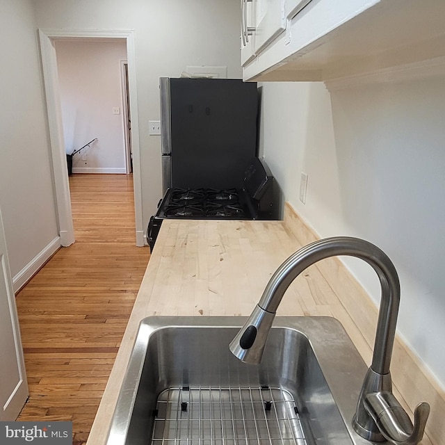 kitchen with stainless steel refrigerator, white cabinetry, sink, black gas range oven, and light hardwood / wood-style floors