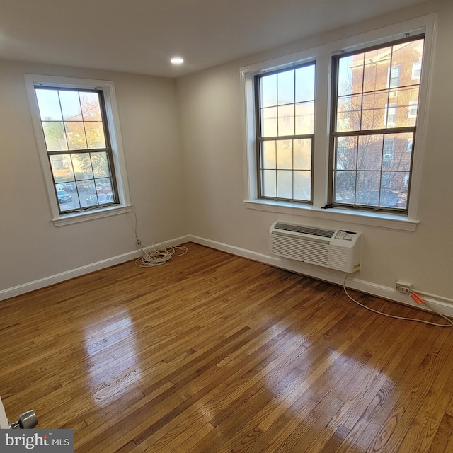 unfurnished room with a wall unit AC, a wealth of natural light, and hardwood / wood-style floors