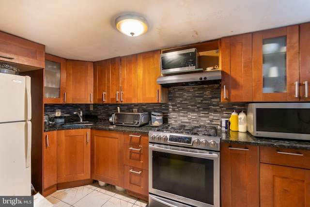 kitchen featuring sink, stainless steel range, range hood, white refrigerator, and dark stone counters