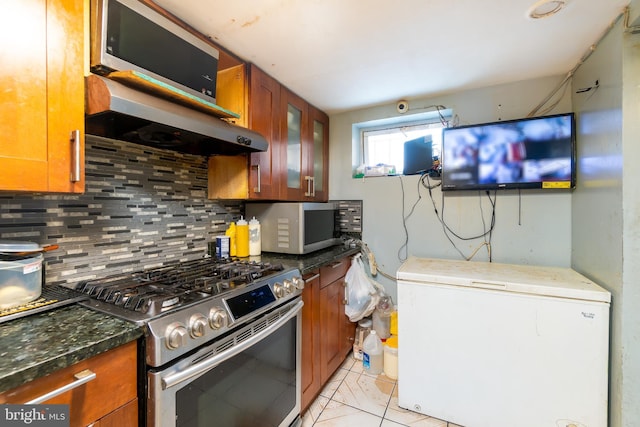 kitchen with refrigerator, backsplash, stainless steel gas range oven, range hood, and light tile patterned flooring