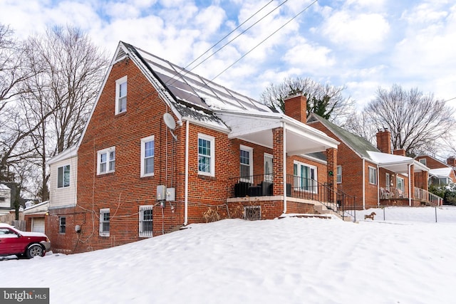 view of snow covered exterior featuring a porch and solar panels