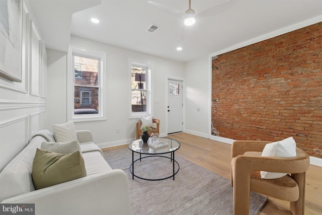 living room with ceiling fan, light hardwood / wood-style floors, and brick wall