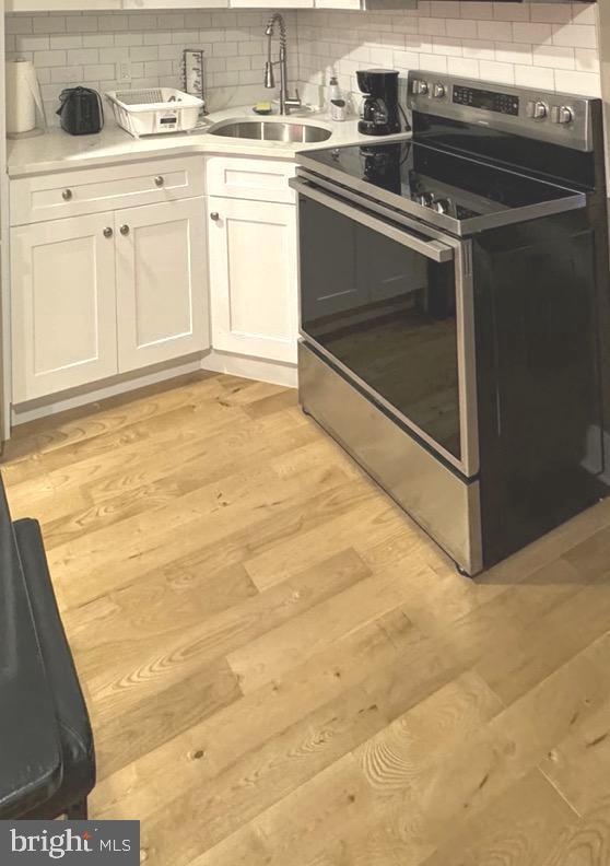 kitchen featuring sink, stainless steel range with electric cooktop, light hardwood / wood-style flooring, decorative backsplash, and white cabinets