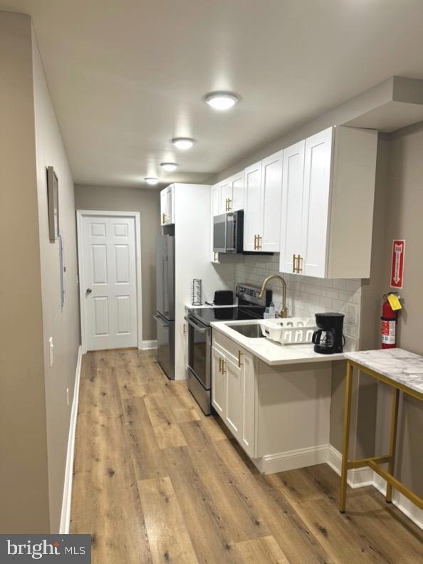 kitchen with sink, white cabinetry, kitchen peninsula, stainless steel appliances, and decorative backsplash