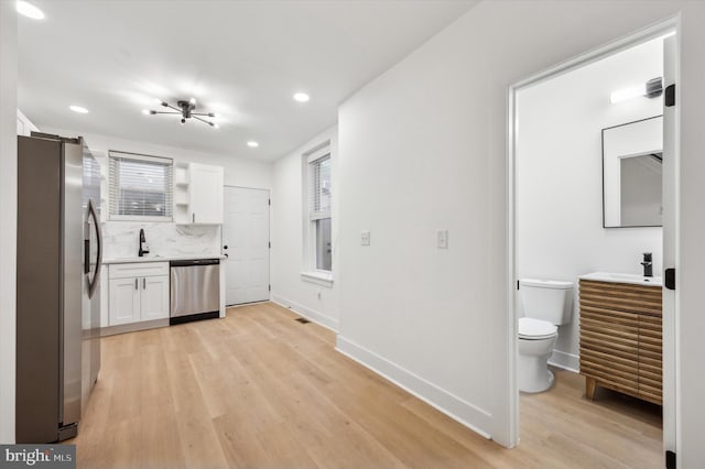 kitchen with white cabinets, sink, appliances with stainless steel finishes, tasteful backsplash, and light hardwood / wood-style floors