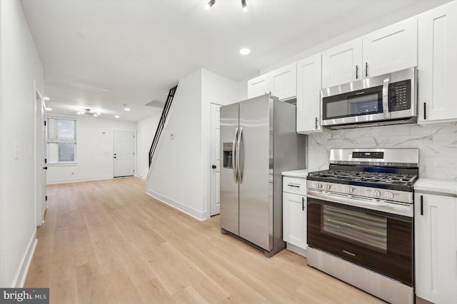 kitchen with backsplash, light hardwood / wood-style flooring, white cabinets, and appliances with stainless steel finishes