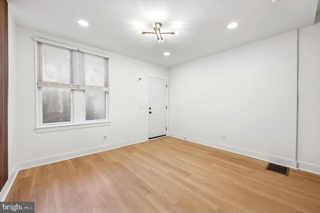 spare room with light wood-type flooring and a chandelier