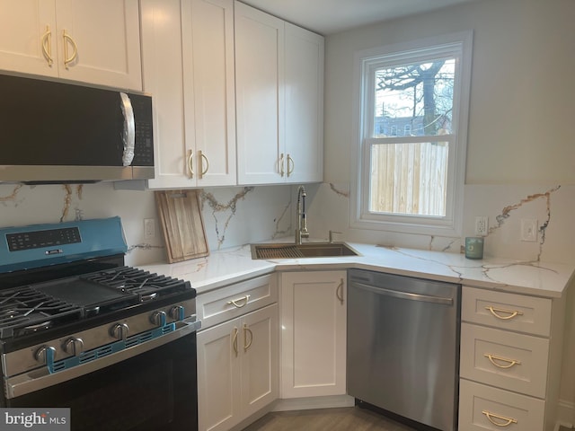 kitchen featuring appliances with stainless steel finishes, backsplash, light stone counters, sink, and white cabinetry