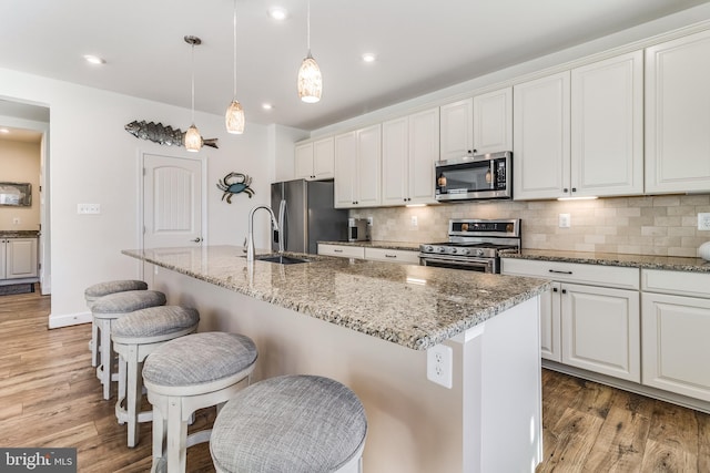 kitchen featuring stainless steel appliances, white cabinetry, and an island with sink