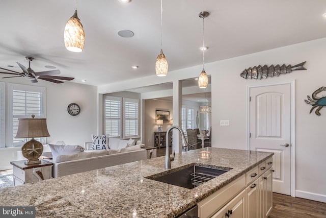 kitchen with ceiling fan, light stone counters, hanging light fixtures, and sink