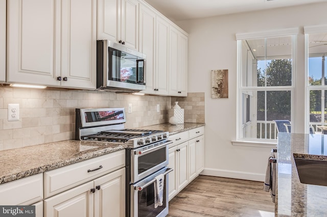 kitchen with white cabinets, light wood-type flooring, tasteful backsplash, light stone counters, and stainless steel appliances