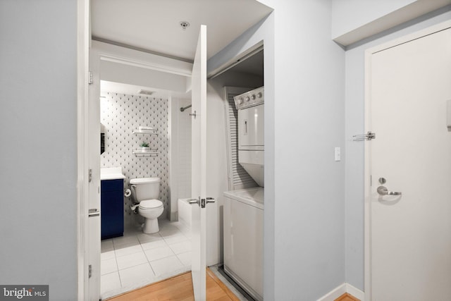 bathroom with tile patterned floors, stacked washer / dryer, a shower, and toilet