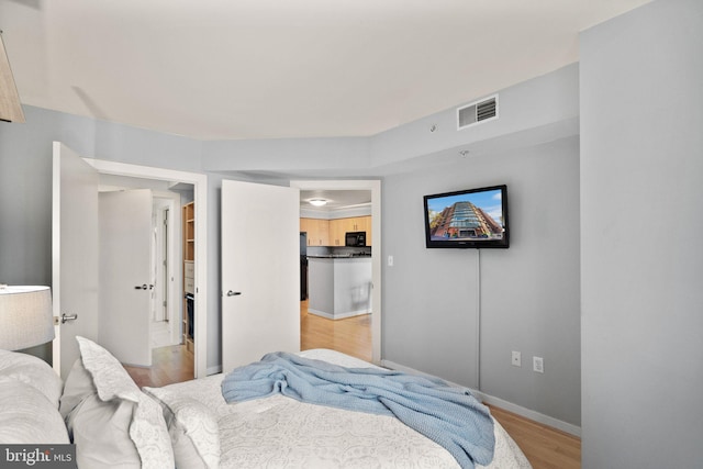 bedroom featuring light hardwood / wood-style floors and black fridge