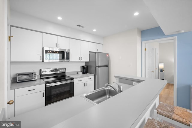 kitchen featuring white cabinetry, sink, stainless steel appliances, light hardwood / wood-style floors, and a breakfast bar