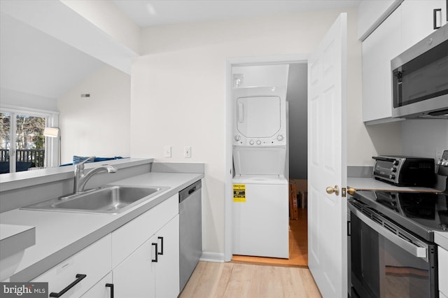 kitchen with light wood-type flooring, stainless steel appliances, sink, white cabinets, and stacked washer and dryer