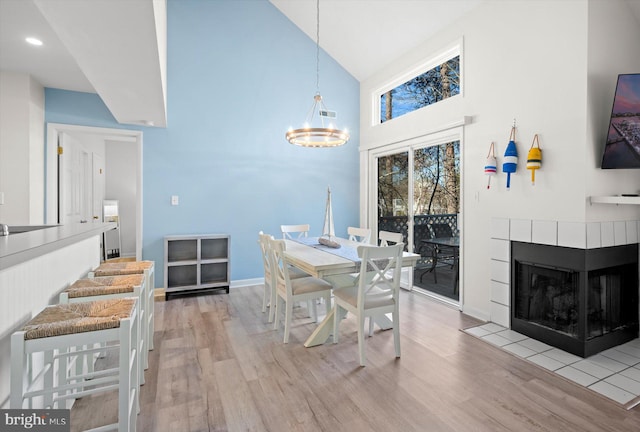 dining space featuring a notable chandelier, light hardwood / wood-style floors, a fireplace, and high vaulted ceiling