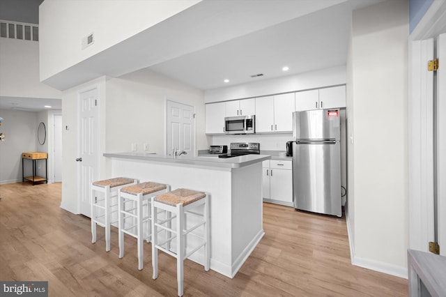 kitchen featuring a breakfast bar, white cabinets, light wood-type flooring, appliances with stainless steel finishes, and kitchen peninsula