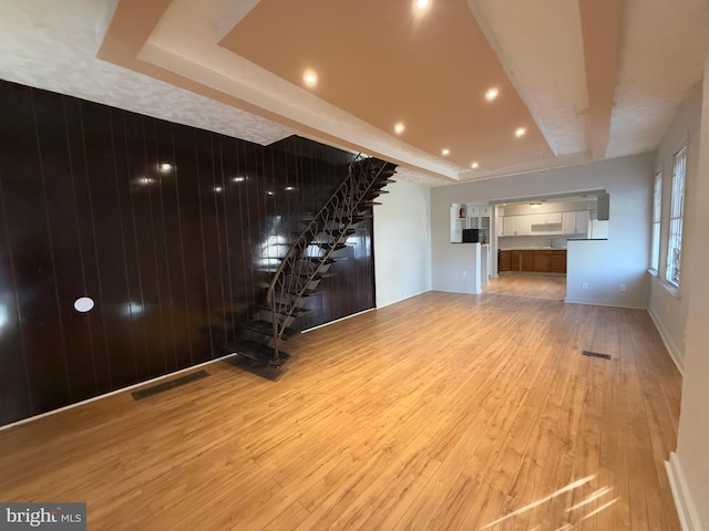 unfurnished living room featuring light wood-type flooring and a tray ceiling