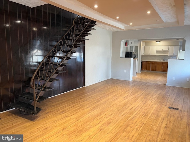 unfurnished living room featuring a tray ceiling, light hardwood / wood-style flooring, and sink