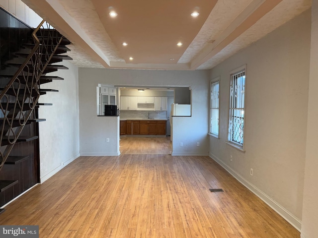 unfurnished living room with a raised ceiling, light wood-type flooring, and sink