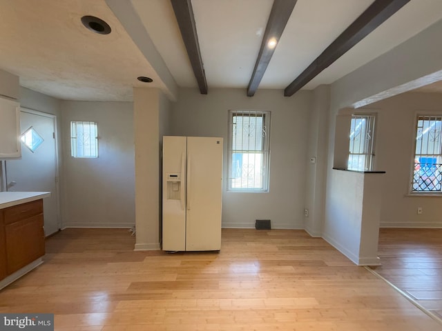 kitchen featuring white refrigerator with ice dispenser, a healthy amount of sunlight, light wood-type flooring, and beamed ceiling