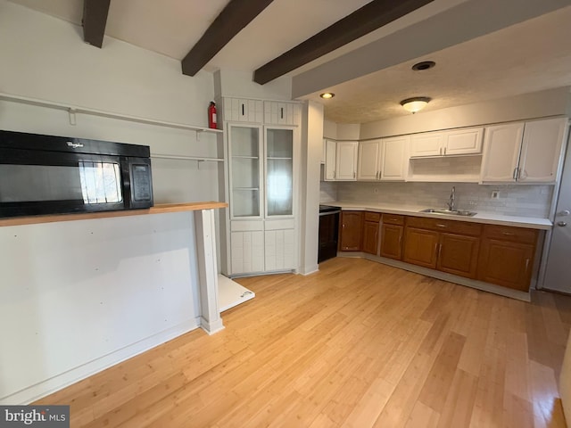 kitchen featuring white cabinetry, sink, beamed ceiling, backsplash, and light hardwood / wood-style floors