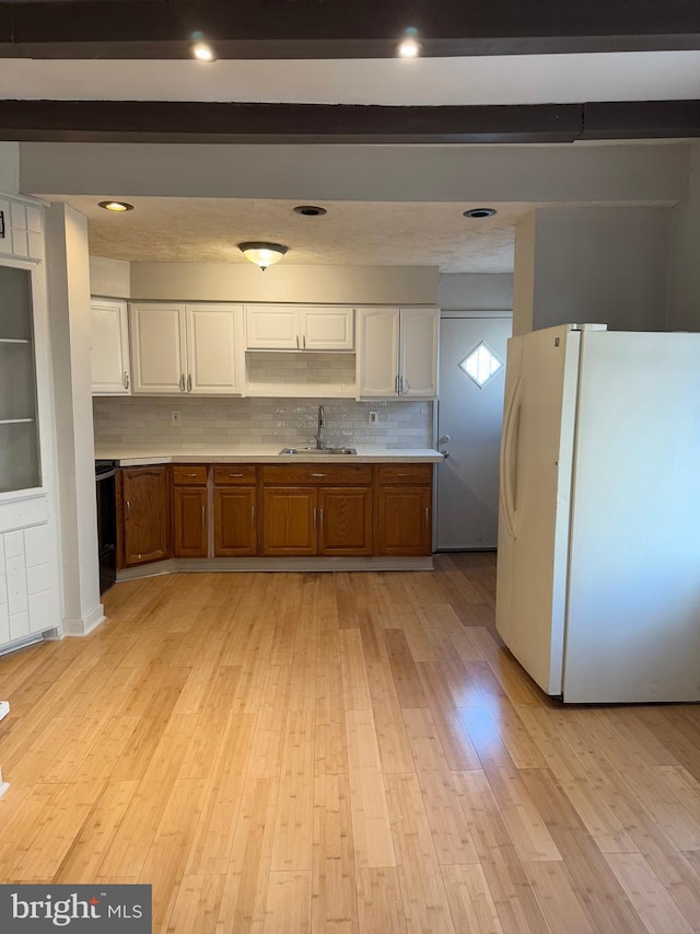 kitchen with backsplash, white refrigerator, sink, light hardwood / wood-style flooring, and beam ceiling