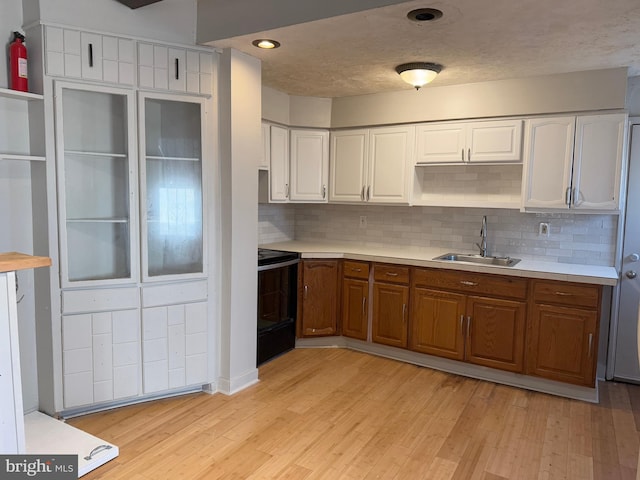 kitchen with stove, backsplash, white cabinets, sink, and light hardwood / wood-style flooring