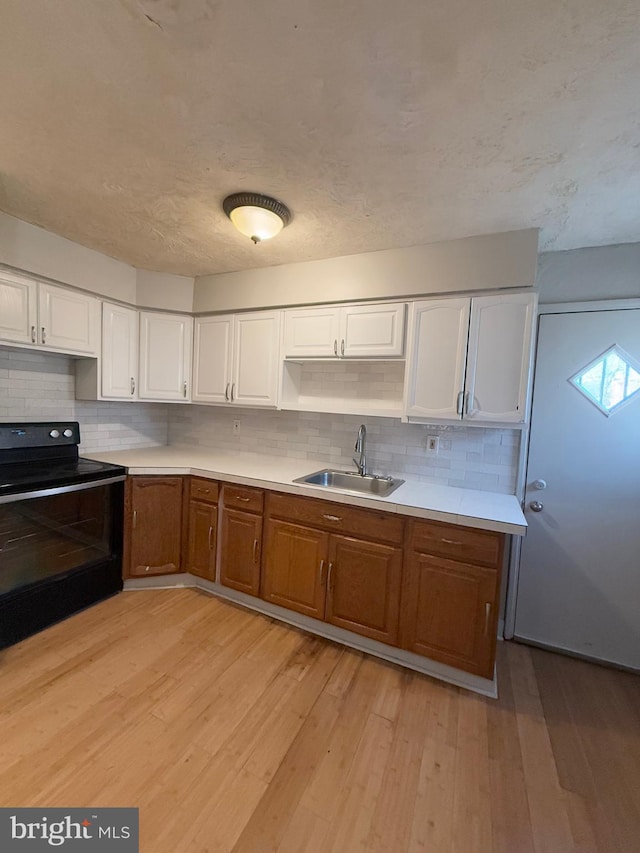 kitchen with a skylight, black range with electric stovetop, sink, light hardwood / wood-style flooring, and white cabinetry