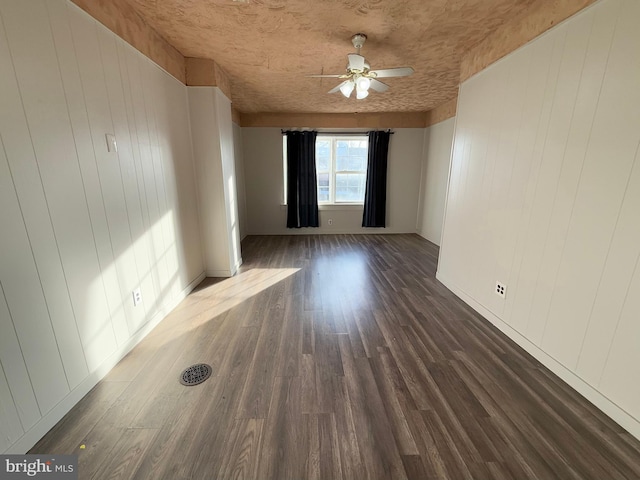 spare room featuring ceiling fan, wooden walls, and dark wood-type flooring