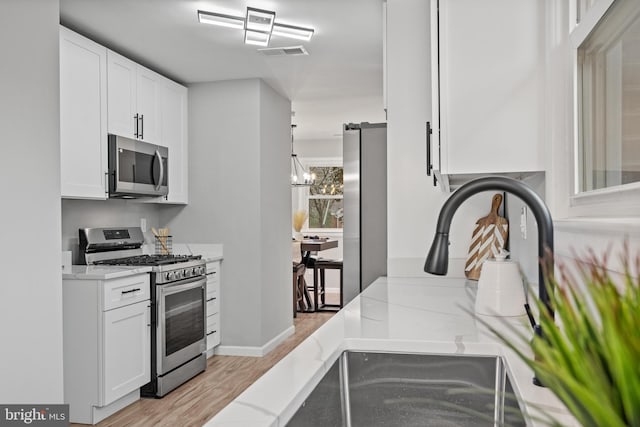 kitchen featuring appliances with stainless steel finishes, light stone counters, an inviting chandelier, light hardwood / wood-style floors, and white cabinetry