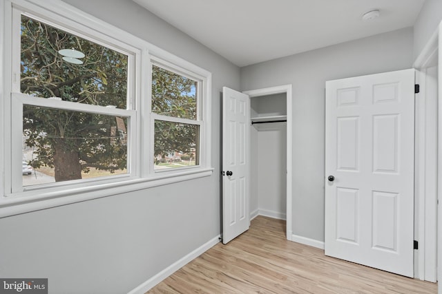 unfurnished bedroom featuring multiple windows, light wood-type flooring, and a closet