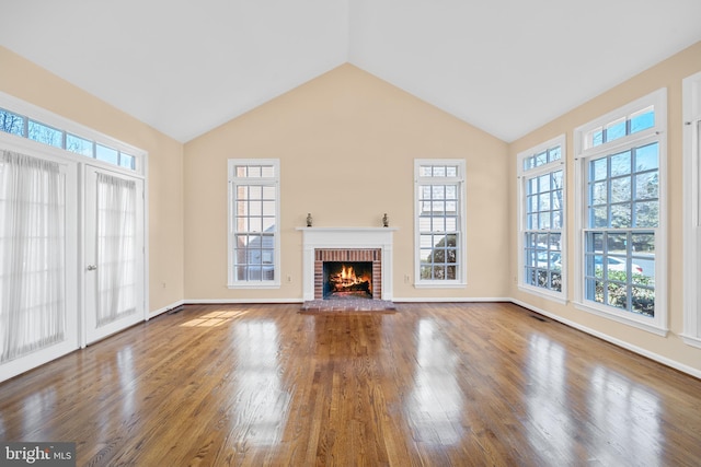 unfurnished living room with lofted ceiling, a brick fireplace, baseboards, and wood finished floors