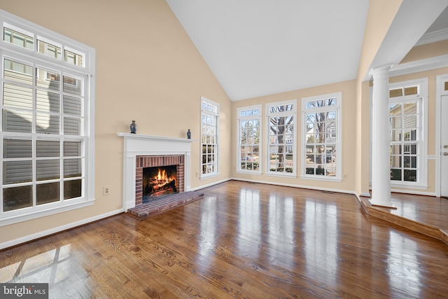 unfurnished living room with ornate columns, a brick fireplace, high vaulted ceiling, and wood finished floors