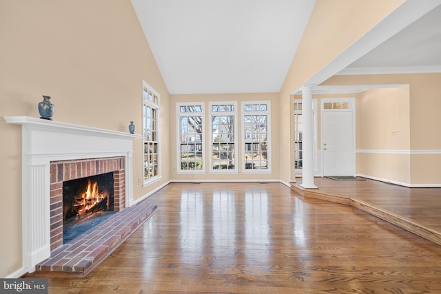 unfurnished living room featuring vaulted ceiling, a fireplace, decorative columns, and wood finished floors