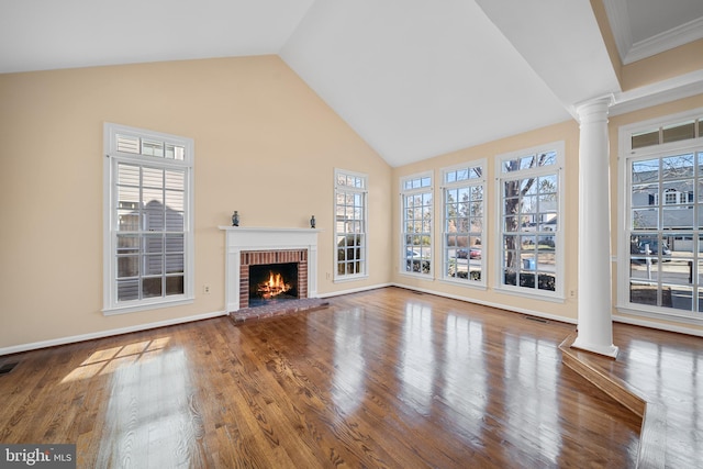 unfurnished living room featuring a brick fireplace, wood finished floors, decorative columns, and a healthy amount of sunlight