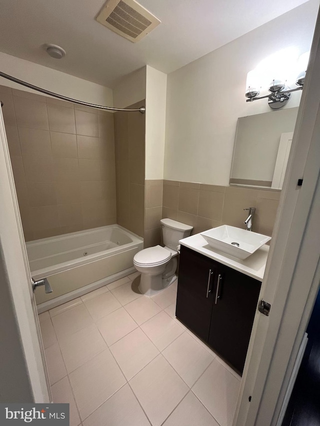 full bathroom with vanity, tile patterned flooring, tiled shower / bath combo, toilet, and tile walls