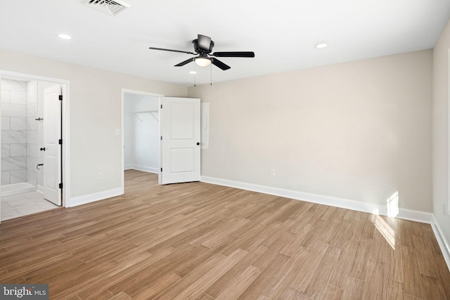 unfurnished bedroom featuring ensuite bathroom, a walk in closet, light hardwood / wood-style flooring, ceiling fan, and a closet