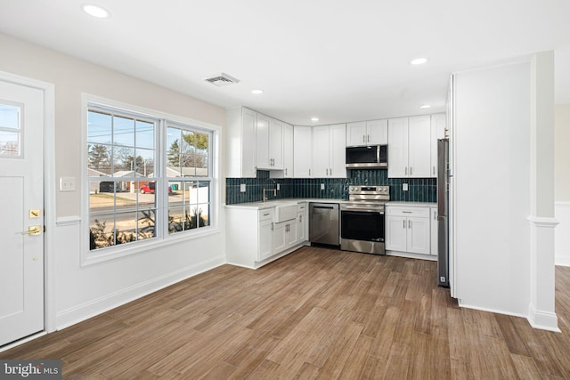 kitchen featuring white cabinetry, sink, stainless steel appliances, backsplash, and light wood-type flooring