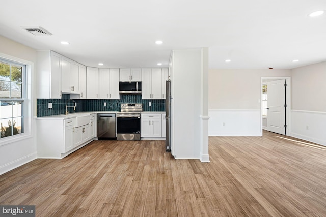 kitchen featuring decorative backsplash, light hardwood / wood-style flooring, white cabinets, and stainless steel appliances