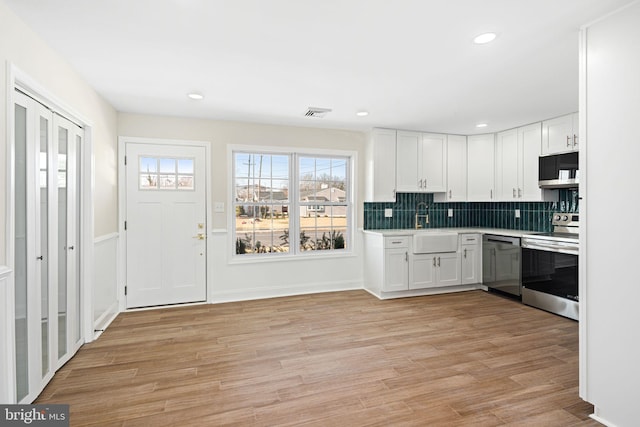 kitchen with tasteful backsplash, white cabinetry, appliances with stainless steel finishes, and light hardwood / wood-style flooring