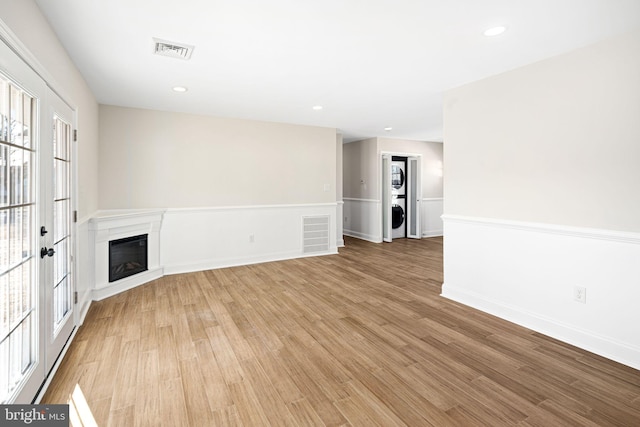 unfurnished living room featuring french doors, light hardwood / wood-style flooring, and stacked washer / drying machine