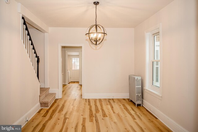 unfurnished dining area featuring radiator heating unit, light hardwood / wood-style floors, and an inviting chandelier