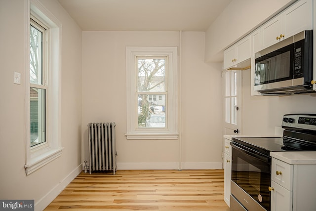 kitchen with appliances with stainless steel finishes, radiator heating unit, light hardwood / wood-style floors, and white cabinetry