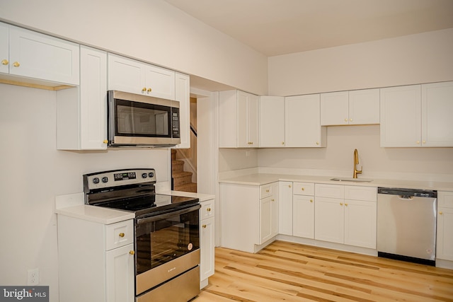 kitchen with stainless steel appliances, white cabinetry, light hardwood / wood-style floors, and sink